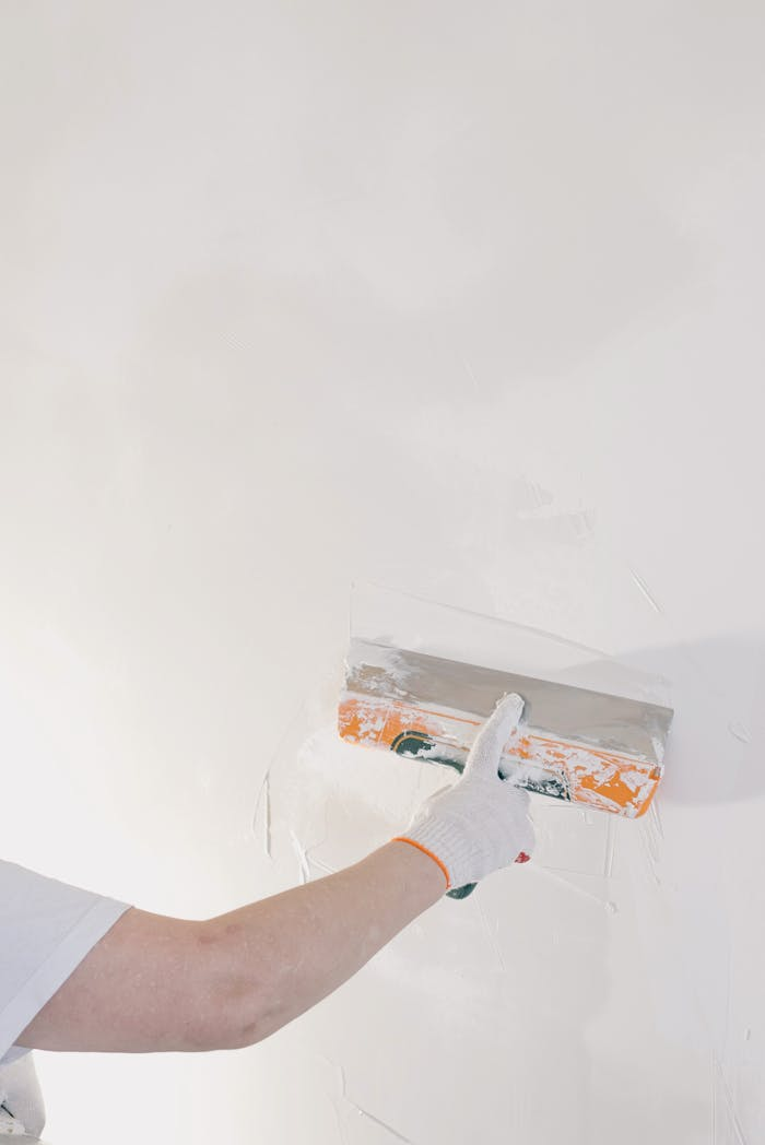Close-up of a gloved hand plastering a wall with a spatula in a home renovation setting.